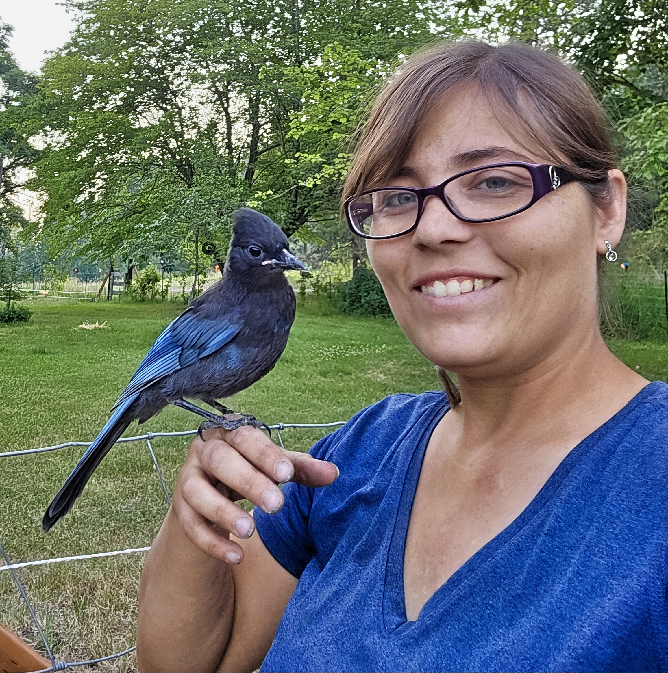 Picture of smiling woman with a stellars jay perched on her hand.